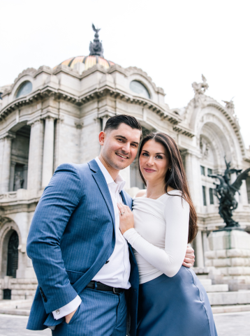 Pareja sonriente posando frente al Palacio de Bellas Artes en la Ciudad de México, en una sesión fotográfica elegante y romántica.
