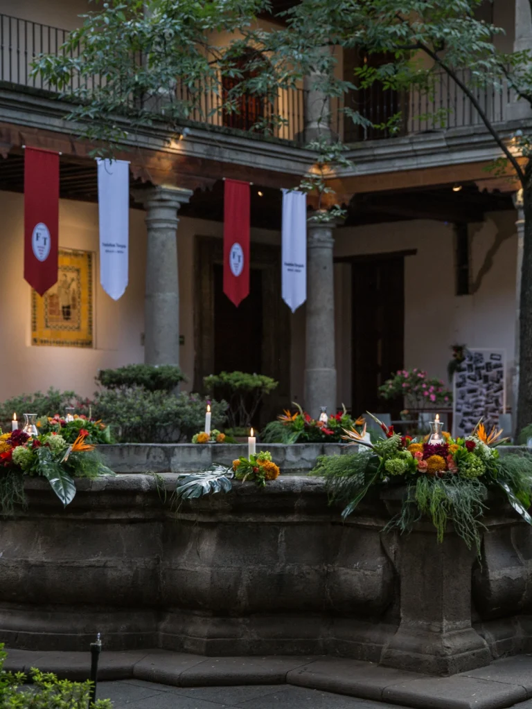Decoración floral en un patio colonial con fuentes adornadas con flores tropicales y velas, destacando un ambiente elegante y tradicional.